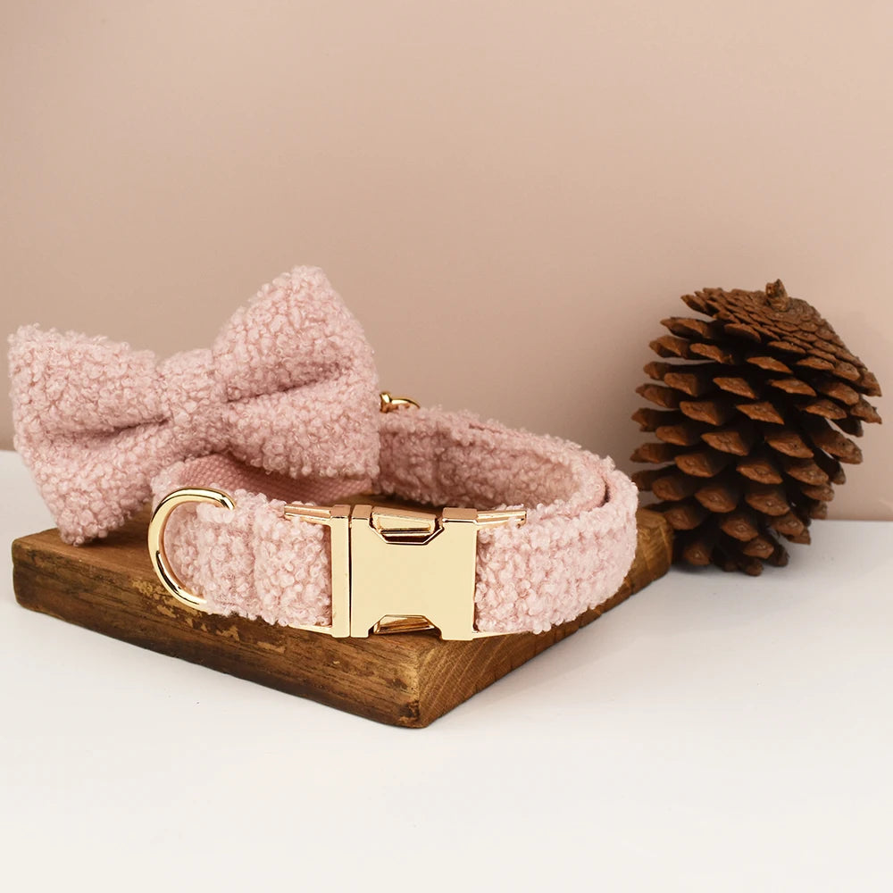 Pink fluffy dog collar with a gold clasp on a wooden tray next to a pine cone.