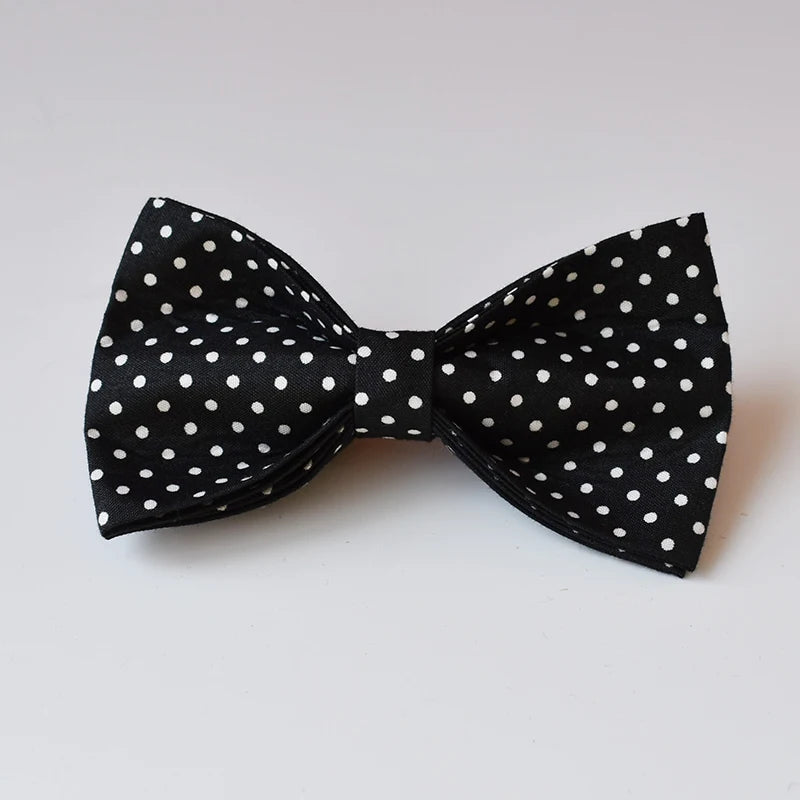 Black bow tie with white polka dots on a light gray background