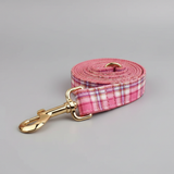 Pink plaid dog leash with gold clip on a gray background