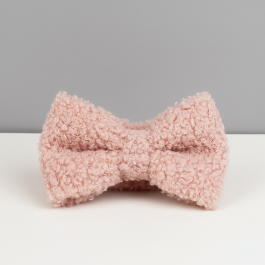 A pink dog bow on a white table with a gray wall behind it