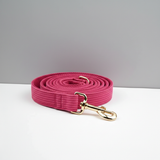 Pink dog leash with gold clasp on a white surface and gray background