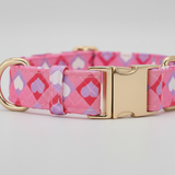 Pink dog collar with heart pattern and gold buckle on a light gray background