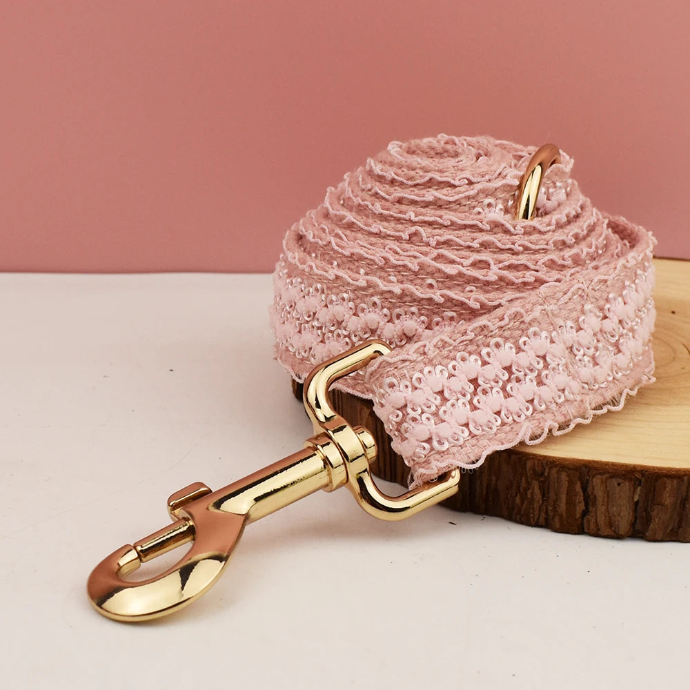 Pink lace dog leash with gold hardware on a wooden block against a pink background