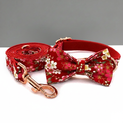 Red floral dog collar, bow tie, and leash set on a white surface with a gray background