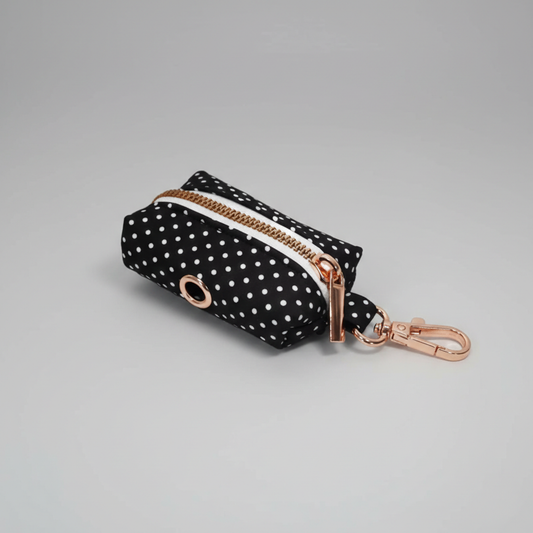 Black polka dot pouch with rose gold zipper and keychain on a gray background