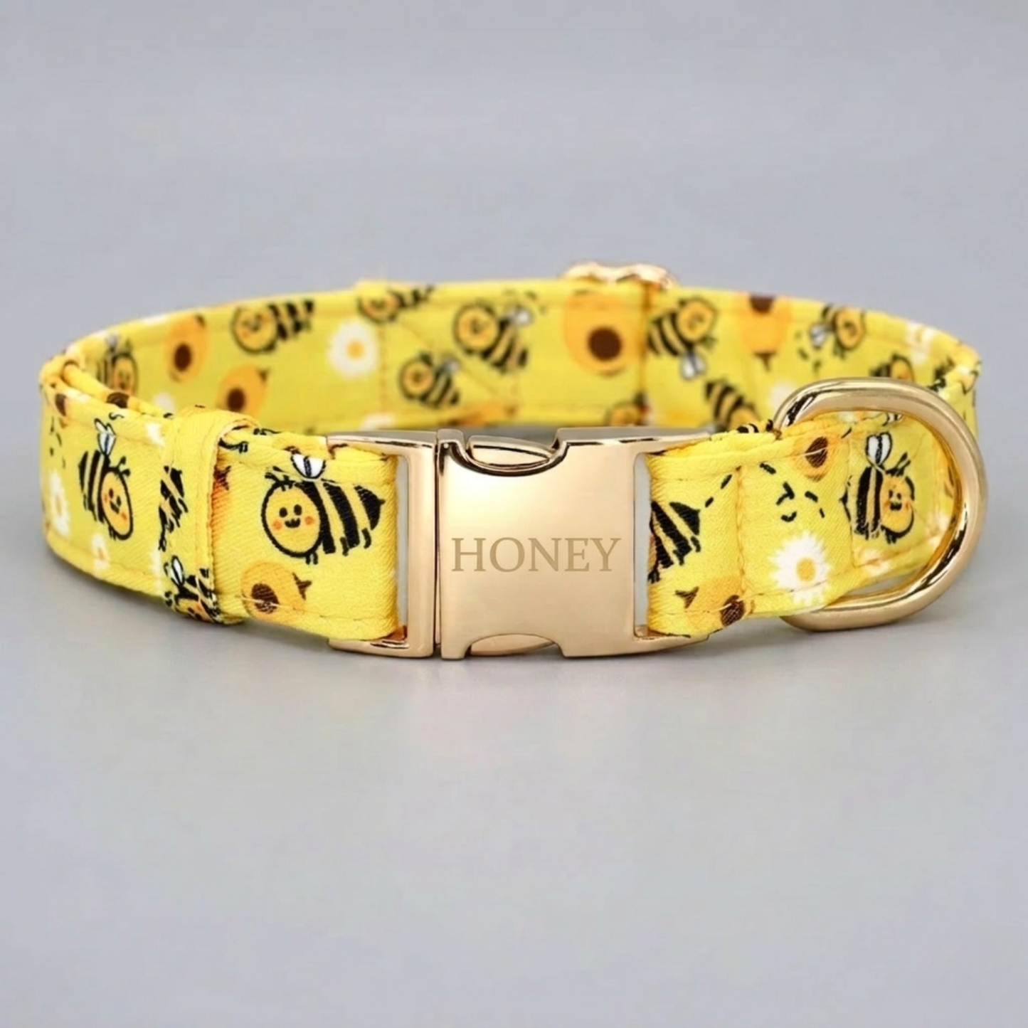 Yellow dog collar with bee pattern and 'Honey' buckle on a light gray background