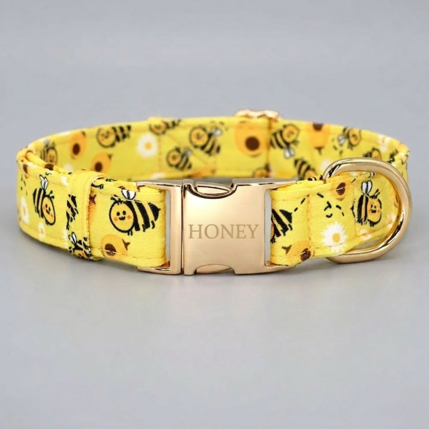 Yellow dog collar with bee pattern and 'Honey' buckle on a light gray background
