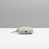 Light green dog waste bag holder with gold hardware on a white surface and gray background