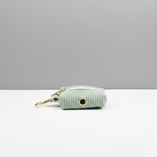 Light green dog waste bag holder with gold hardware on a white surface and gray background