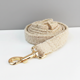 Beige dog leash with gold clip on a white surface